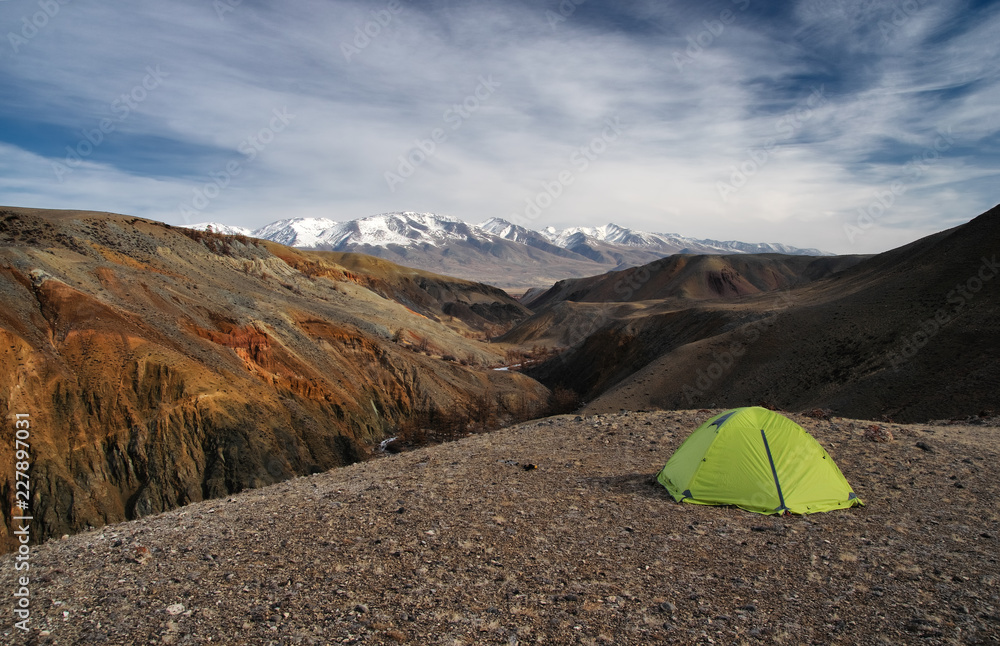 Camp tent in dramatic dark desert steppe on a highland mountain plateau on a horizon snow peaks