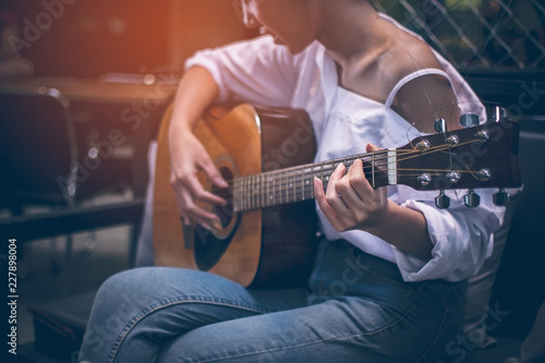 Asian girls wearing white shirts and jeans. She is sitting on a black couch is currently vacationing by playing guitar in a coffee shop.