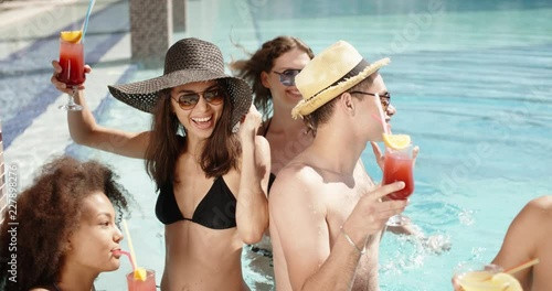 Group of multiethnic friends enjoying theit time in swimming pool, chatting and drinking cocktails. Vacation concept 4k photo