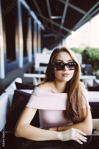 Portrait of a young pretty woman in a sunglasses sits in summer cafe.