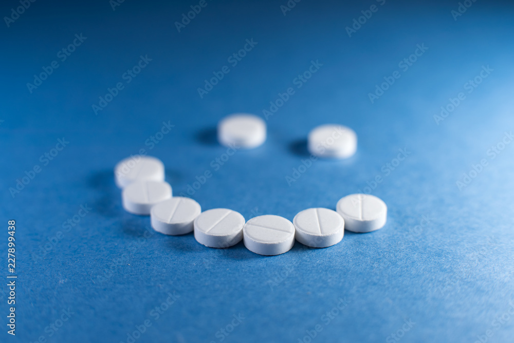 Happy smile made from white pills on blue background