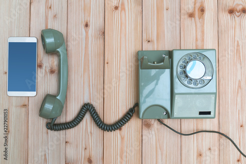 Retro rotary telephone or vintage phone with cable and new cell phone or smart phone on wood table, top view with copy space, technology progress concept.