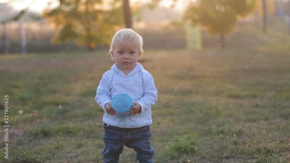 Little toddler boy, eat dry fruits from a smart snack box with silicon top in a park on sunset Little toddler boy, eat dry fruits from a smart snack box with silicon top in a park on sunset