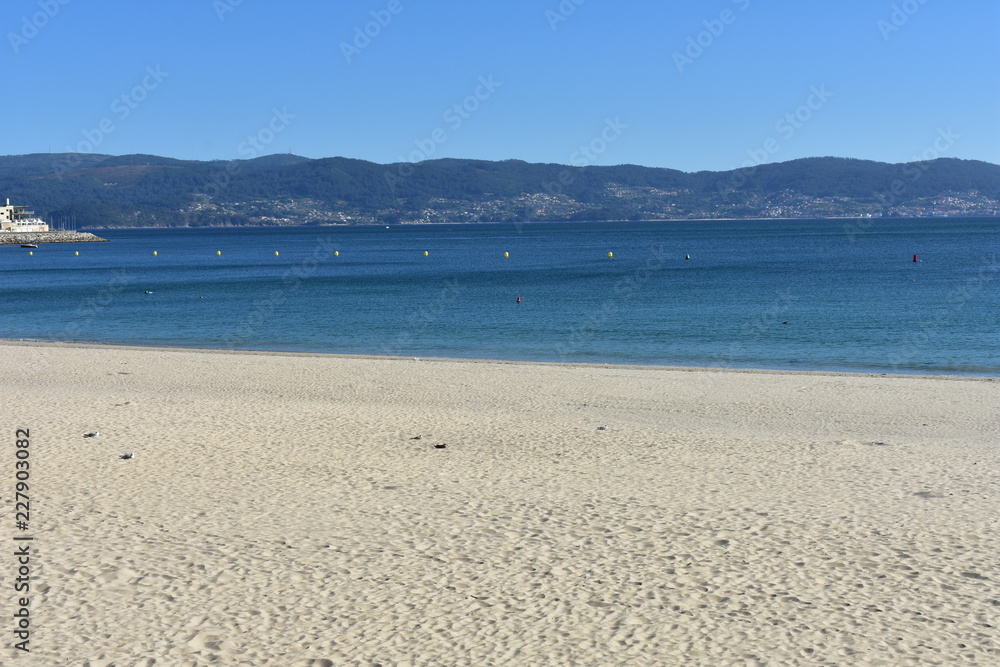 Beach with bright sand and clear water. Sunny day, blue sky. Sanxenxo, Rias Baixas, Spain.