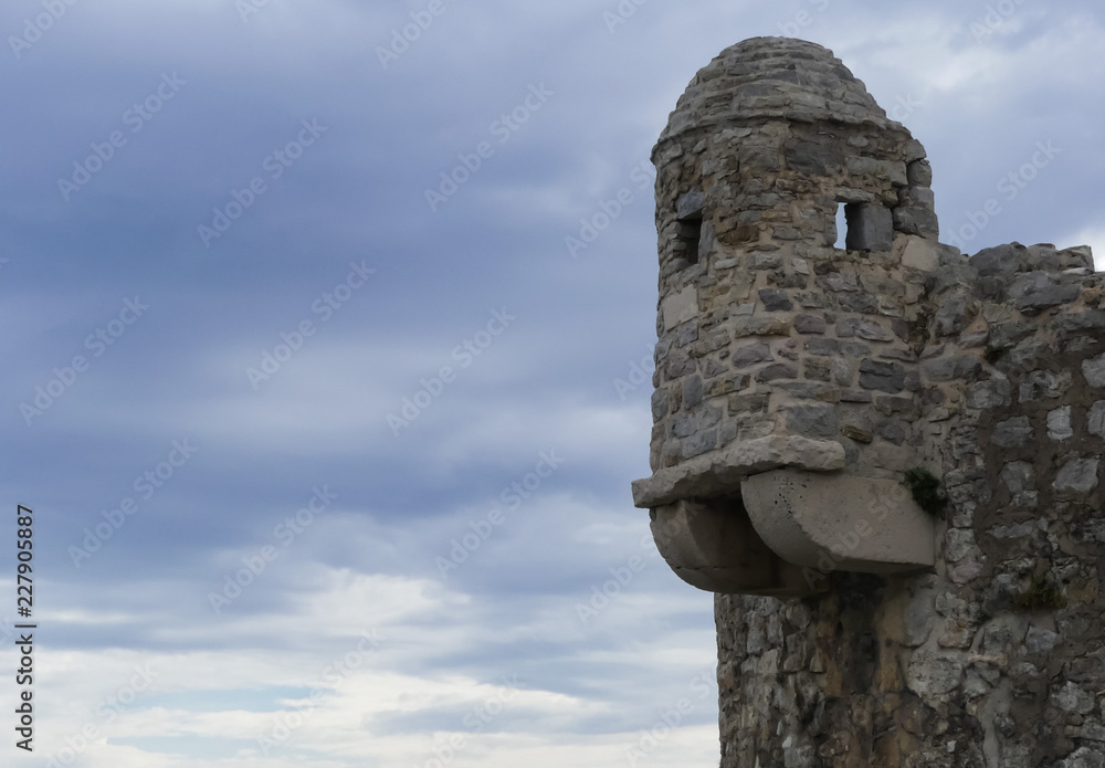 Public view profile of ancient roofed stone watch tower on walled town of Budva. Buttressed with darkening cloudy sky.  Montenegro.