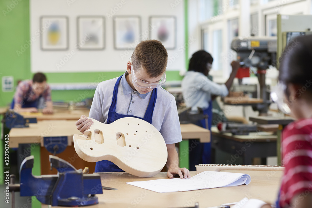 Obraz premium Male High School Student Building Guitar In Woodwork Lesson