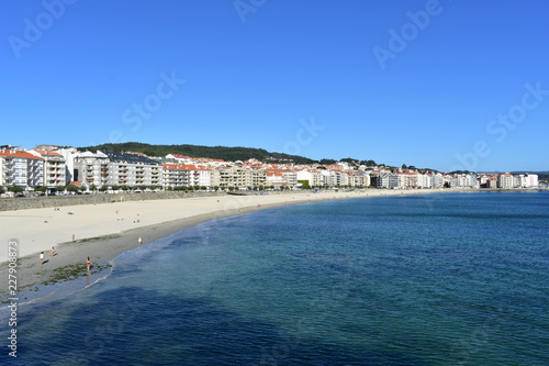 Small coastal village with beach and promenade. Turquoise and clear water, bright sand, blue sky. Sanxenxo, Rias Baixas, Galicia, Spain.