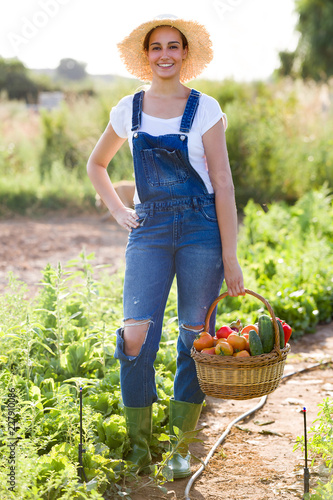 Beautiful young smiling woman holding basket with fresh vegetables from the garden looking at the camera.