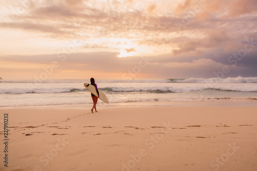 Surf girl go to ocean for surfing. Surfer woman on a beach at sunset