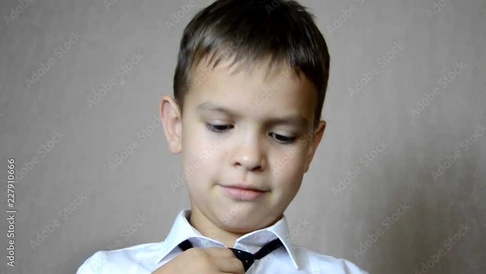 Young businessman the boy is wearing a white shirt and tie. schoolboy. Concept of personal growth or learning. Button buttons. straightens tie. Fashion portrait of little handsome boy in office Young businessman the boy is wearing a white shirt and tie. schoolboy. Concept of personal growth or learning. Button buttons. straightens tie. Fashion portrait of little handsome boy in office