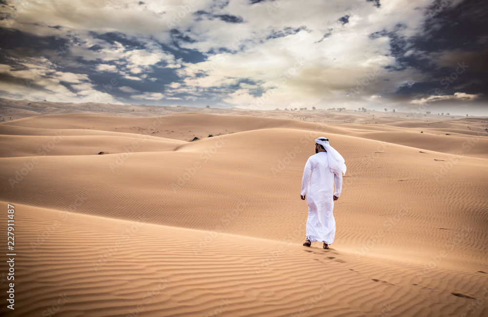 Naklejka premium Arabski mężczyzna chodzący po pustyni z tradycyjnymi ubraniami emiratów