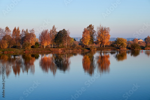 Autumn trees reflect the lake.