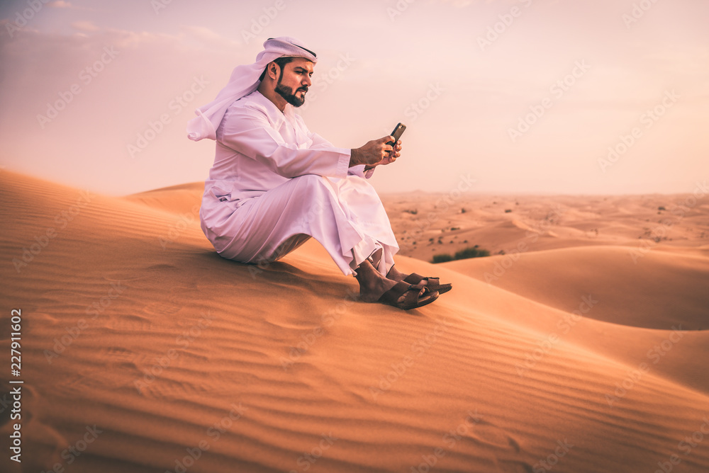 Fototapeta premium Arabski mężczyzna chodzący po pustyni z tradycyjnymi ubraniami emiratów