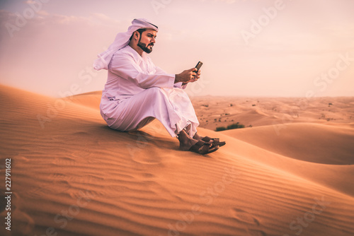 Arabic man with traditional emirates clothes walking in the desert photo