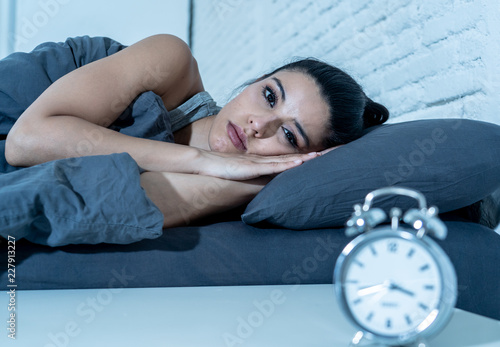 Attractive woman staring at alarm clock trying to sleep feeling stressed depressed and sleepless photo
