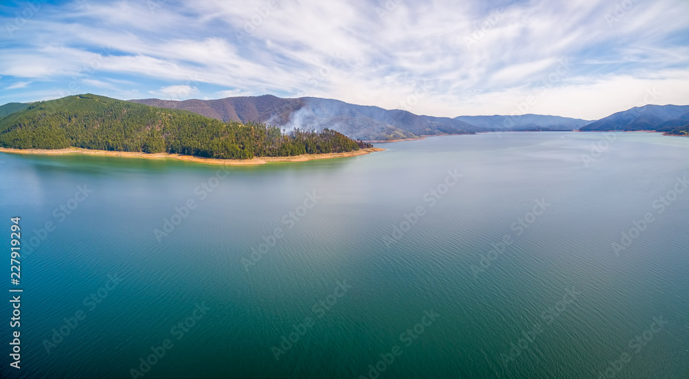 Aerial panorama of smoke rising from forest among beautiful scenic hills on lake shore