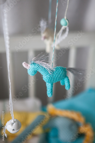 Blue crocheted unicorn toy hanging above baby cot
