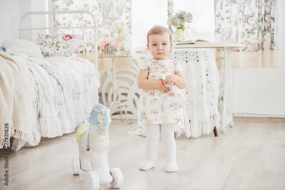 Beautiful little girl playing toys. Blue-eyed blonde. White chair. Children's room. Happy small girl portrait. Childhood concept Beautiful little girl playing toys. Blue-eyed blonde. White chair. Children's room. Happy small girl portrait. Childhood concept