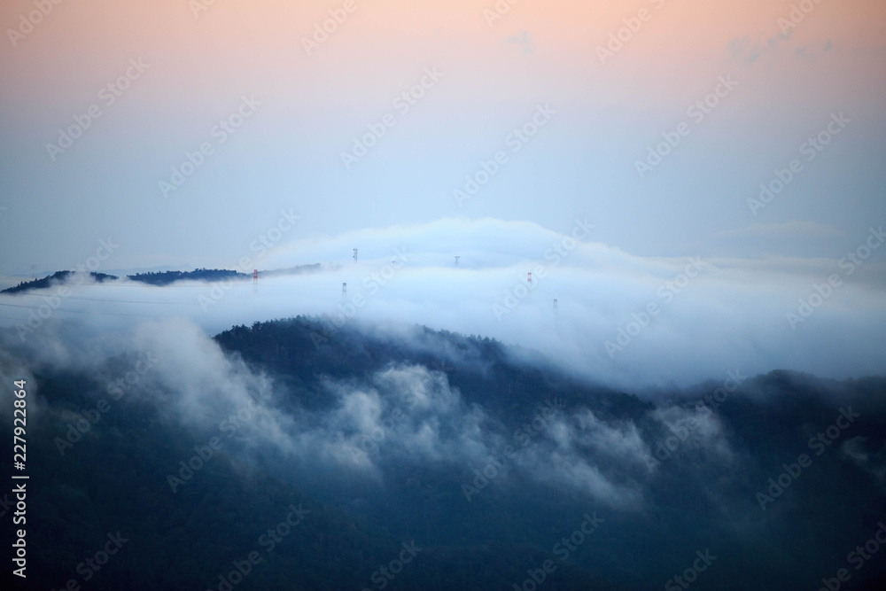Electrical towers peak out from morning fog as sky glows orange with first signs of sunrise Electrical towers peak out from morning fog as sky glows orange with first signs of sunrise
