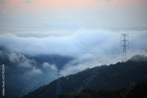 Towers carrying high voltage electrical lines through mountains and fog at sunrise