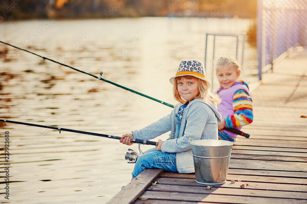 Little girls fishing on the lake, sitting on a wooden pontoon Little girls fishing on the lake, sitting on a wooden pontoon