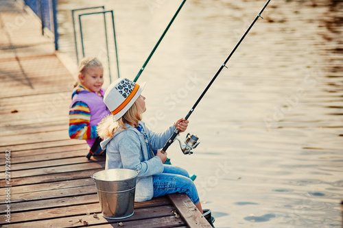 Two little girls fishing on the lake on a sunny morning.