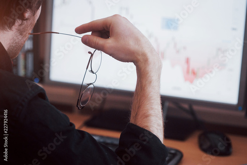 Analyzing data. Close up of a young businessman who holds glasses and looks at the gff while working in a creative office