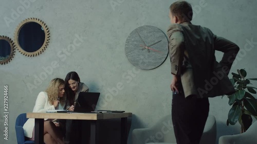 Two lazy unproductive female office workers browsing social media on internet with smart phone during work hours. Careless female coworkers avoiding job and networking with cellphone caught by manager