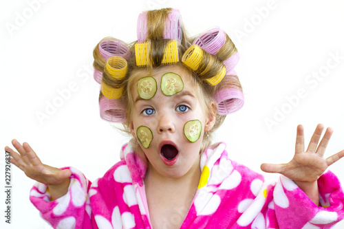 Девочка в банном розовом халате с бигудями и кусочками огурцов на лице. photo
