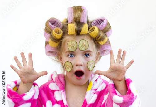 Девочка в банном розовом халате с бигудями и кусочками огурцов на лице. photo