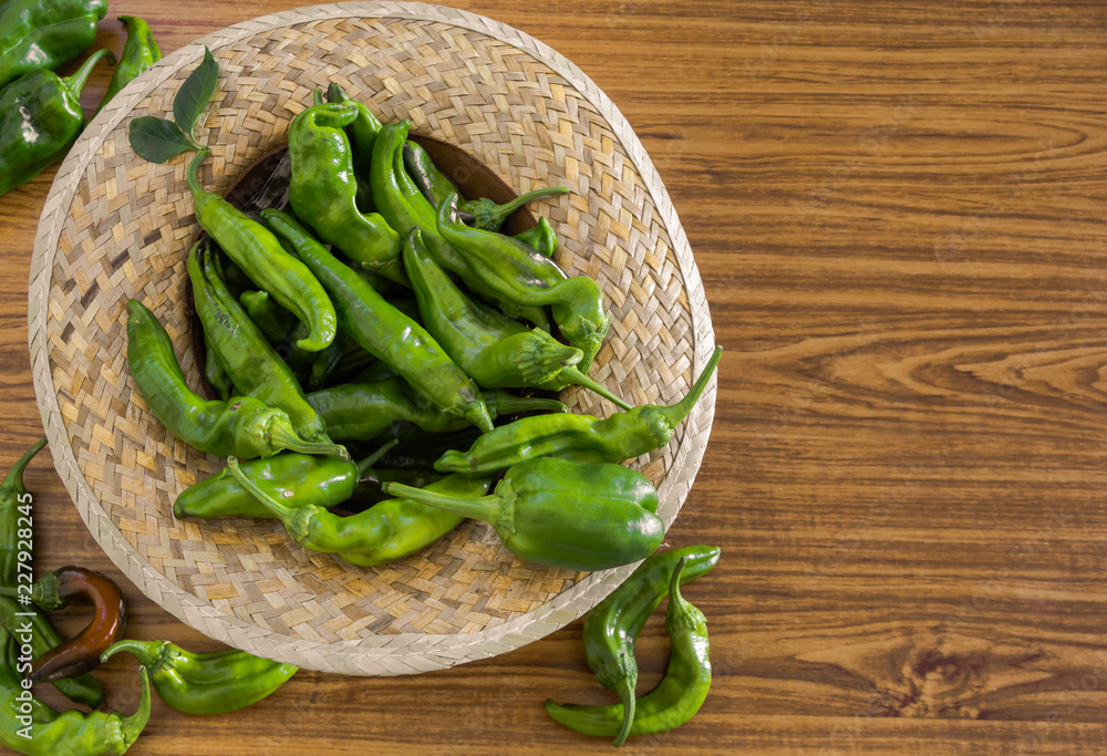 Straw hat of a farmer filled with organic green peppers freshly collected on a wooden background. Top view of vegetables, copy space in right side. Straw hat of a farmer filled with organic green peppers freshly collected on a wooden background. Top view of vegetables, copy space in right side.