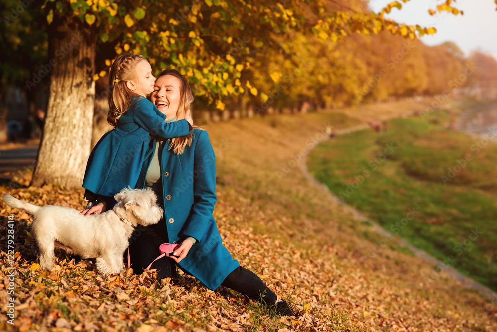 Mother and daughter on autumn walk with dog. Happy loving family having fun. Small white dog and family enjoying together outdoors. Family, pet and lifestyle concept. Mother and daughter on autumn walk with dog. Happy loving family having fun. Small white dog and family enjoying together outdoors. Family, pet and lifestyle concept.