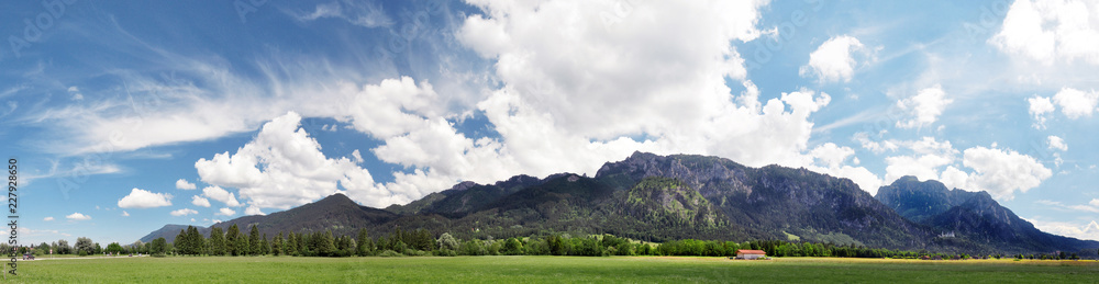 Panoramic view of Alps, Bavaria. Beautiful peaceful landscape, summertime in Bavaria. Blue sky with some white clouds, green meadows and alpine mountains. Neuschwanstein castle on a right side of the 