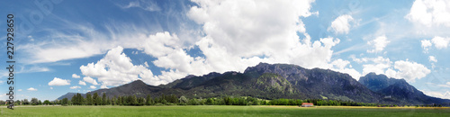 Panoramic view of Alps, Bavaria. Beautiful peaceful landscape, summertime in Bavaria. Blue sky with some white clouds, green meadows and alpine mountains. Neuschwanstein castle on a right side of the 