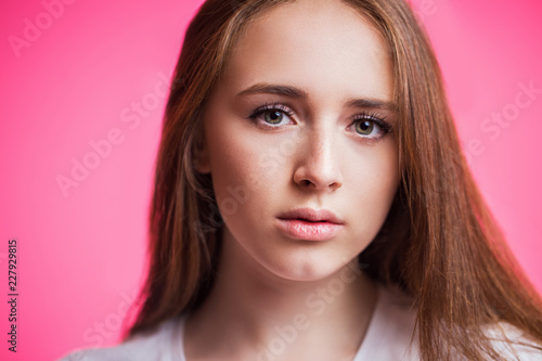 Horizontal close-up portrait of beautiful young girl on pink background. A woman looks at the camera with a piercing gaze