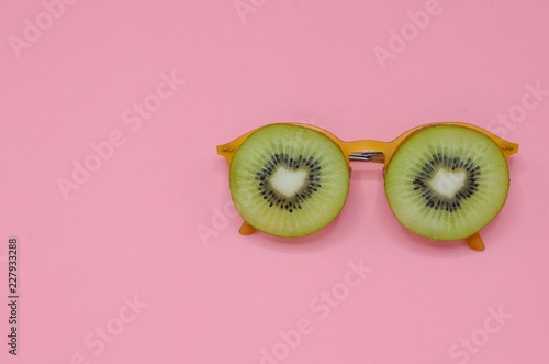 Two slice green kiwi fruits put on yellow sunglasses set as face with eyes photo isolated on pink background for summer time with space for text. photo