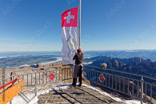 Waiter raises The Swiss Flag at restaurant Old Säntis with sunny views of Appenzell Alps and Rhine Valley, Switzerland
