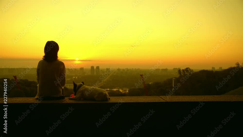 girl with her french bulldog enjoy the sunrise. Girl wears a white sweater, dog wears a blur collar. Dog is bored and doesn't play with its pink balloon. girl with her french bulldog enjoy the sunrise. Girl wears a white sweater, dog wears a blur collar. Dog is bored and doesn't play with its pink balloon.