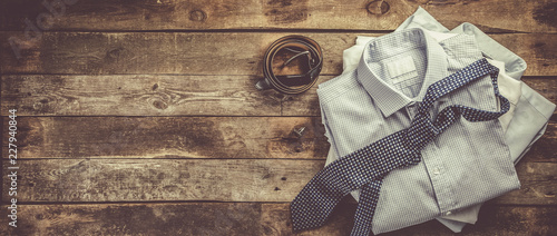Selection of male clothes - stack of folded shirts, tie, belt, cufflinks, rustic wood background