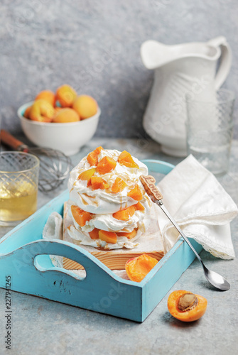 Homemade refined and gentle dessert Pavlova made from meringue, cream and sliced fresh apricots on a blue wooden tray. Close up photo