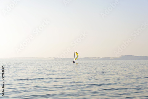 Sailboat with yellow blue striped sail in the sea