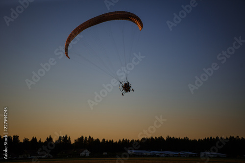 Paratrayke flight, paraglider in the sky at sunset. The wing of a parachute with a paraglider cabin flies across the sky in the setting sun