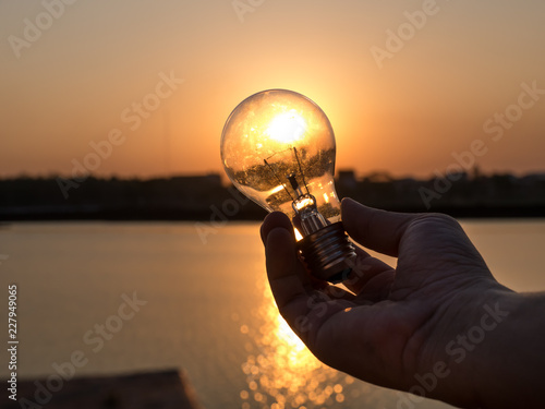 Finger holding light bulb on sunset background, image silhoutte background,