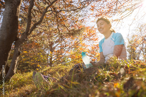 Junge sportliche Frau sitzt im Gras, Blätterdach aus bunten Blättern, Herbst