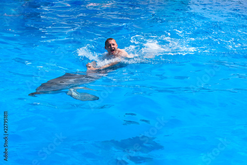 A young man is riding dolphin, boy swimming with dolphin in blue water in water pool, sea, ocean, dolphin saves a man