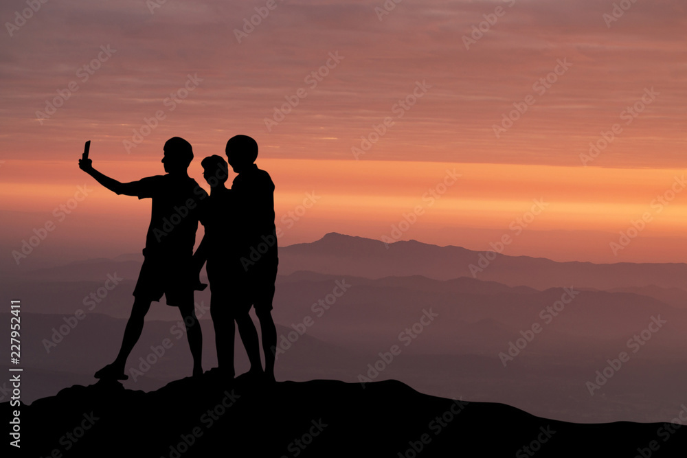 silhouette of people taking selfie at the cliff on mountains with sunset in the evening