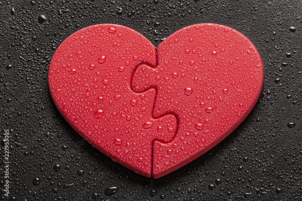 Obraz premium Two Halves of One Heart. Two pieces of a heart-shaped jigsaw puzzle lying on a black colored background, all of which are covered with water drops.