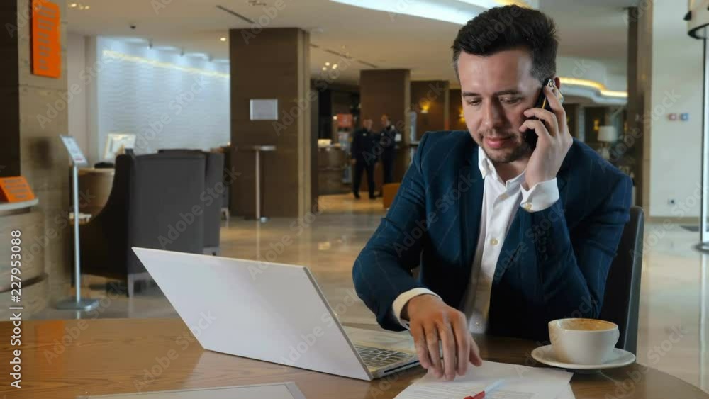 Man working on notebook and calling by smartphone during business trip in hotel Man working on notebook and calling by smartphone during business trip in hotel
