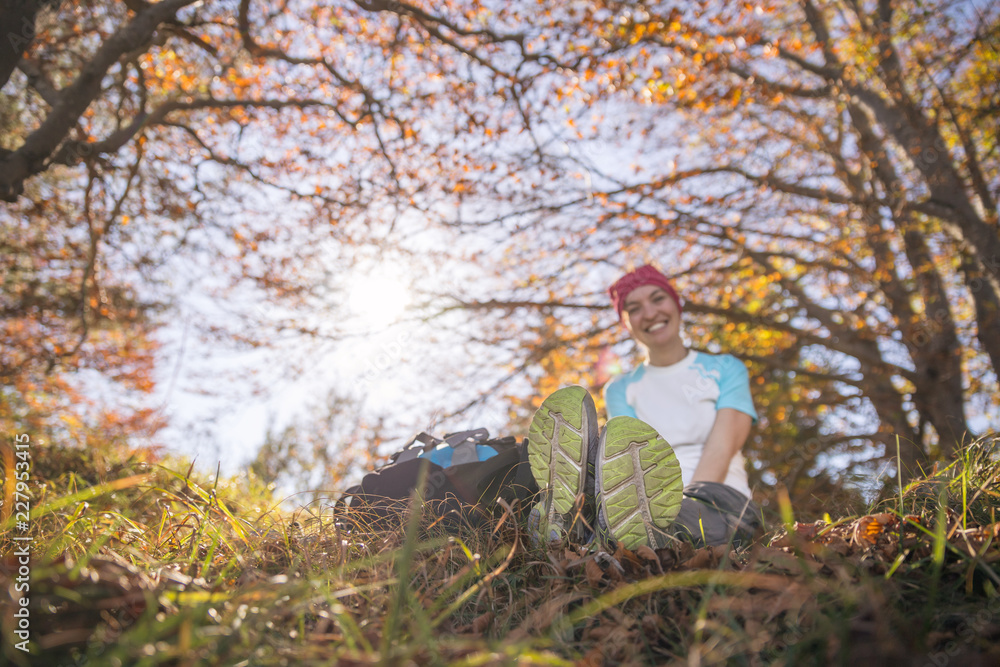 Junge sportliche Frau sitzt im Gras, Blätterdach aus bunten Blättern, Wanderschuhe im Vodergrund, Herbst Junge sportliche Frau sitzt im Gras, Blätterdach aus bunten Blättern, Wanderschuhe im Vodergrund, Herbst
