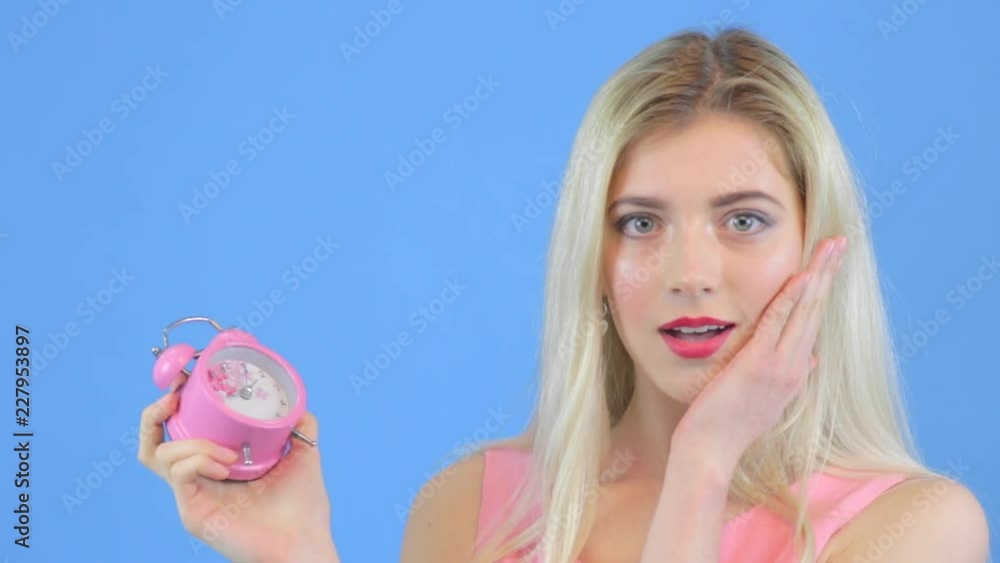 Blond young woman looks at alarm clock Blond young woman looks at alarm clock
